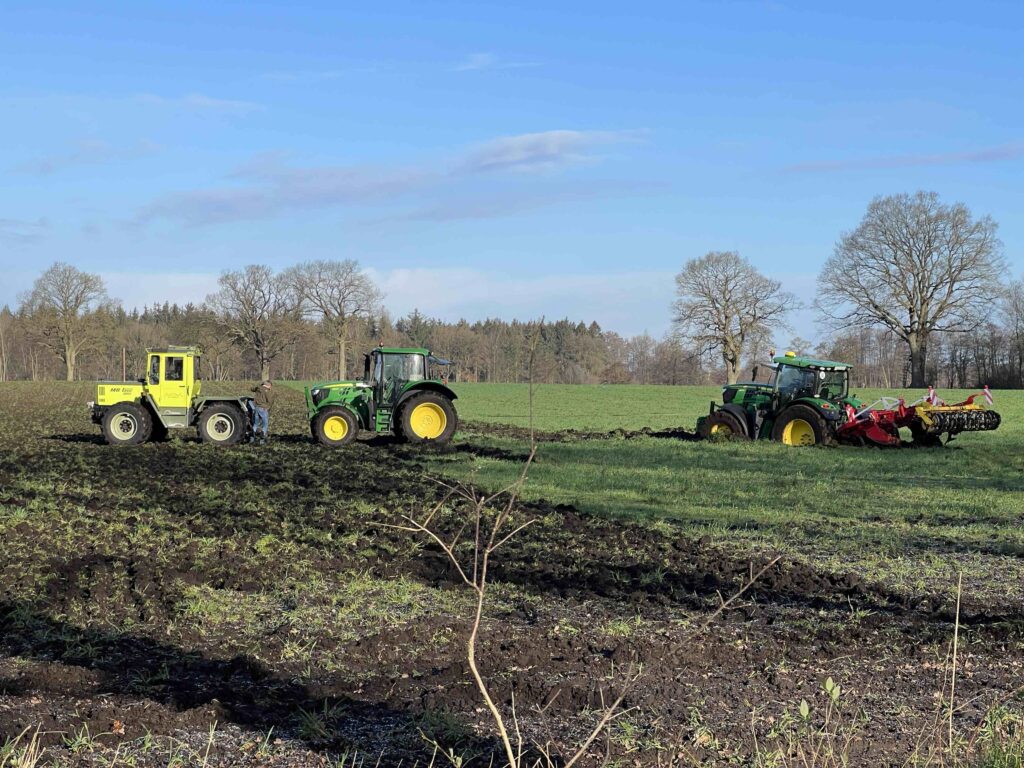 Traktor steckt im Acker fest und wird von zwei weiteren Traktoren an den Haken genommen