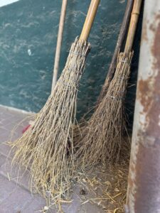 Nahaufnahme von zwei Reisigbesen, die vor einer grüner Wand steht