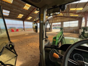 John Deere 6 M mit angehängter Hebebühne in Longierhalle zur Reparatur der Bewässerungsanlage