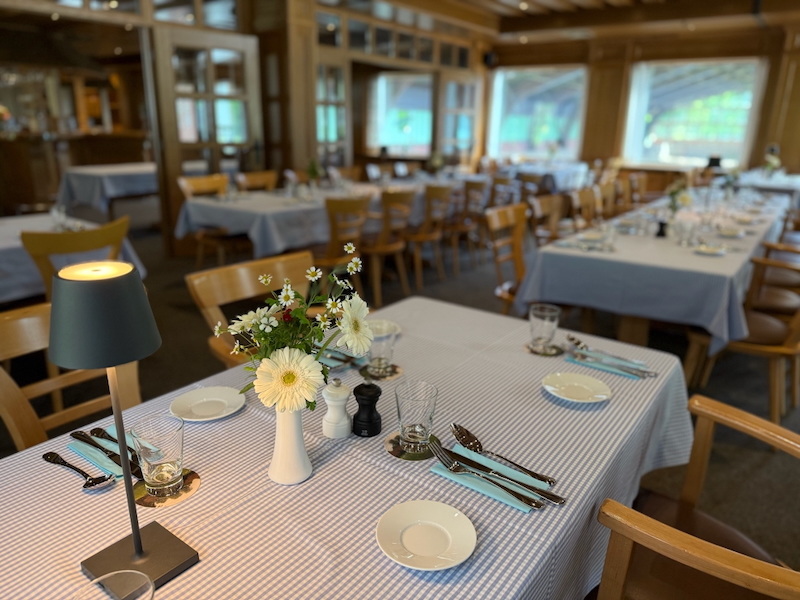 Eingedeckter Veranstaltungsraum mit blau-karierten Tischdecken und frischer Blumendeko
