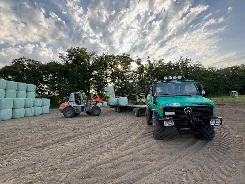 Atlas Radlader entlädt Unimog mit angehängtem Ballenwagen