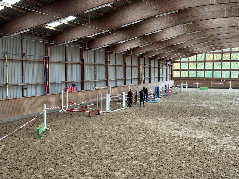 Innenaufnahme der Reithalle auf Gut Tangstedt beim Aufbau zum Freispringen mit Hindernissen, Sprungstangen und mehreren Personen in der Vorbereitung.