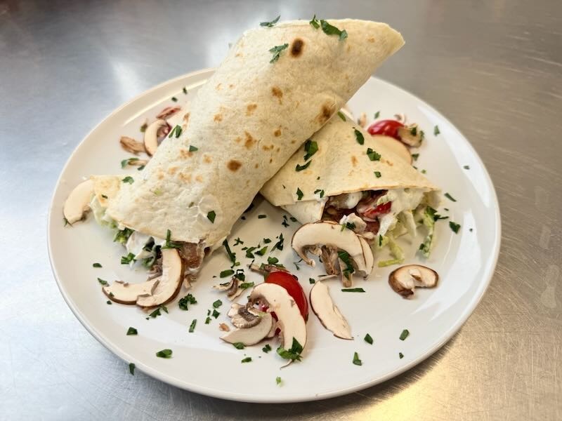 Caesar-Wrap mit Hähnchen, frischem Salat, Tomaten und Champignons, angerichtet auf einem Teller in der Hofküche auf Gut Tangstedt.