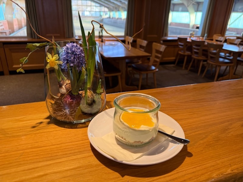 Cremiger Cheesecake im Glas mit fruchtigem Orangen-Topping, serviert neben einer frühlingshaften Hyazinthe im Restaurant.