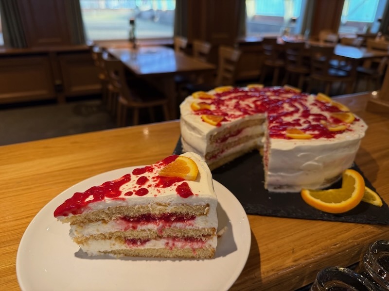 Hausgemachte Himbeer-Sahne-Torte mit fruchtiger Glasur und Orangenspalten, präsentiert als ganzes Stück und angeschnittene Torte.
