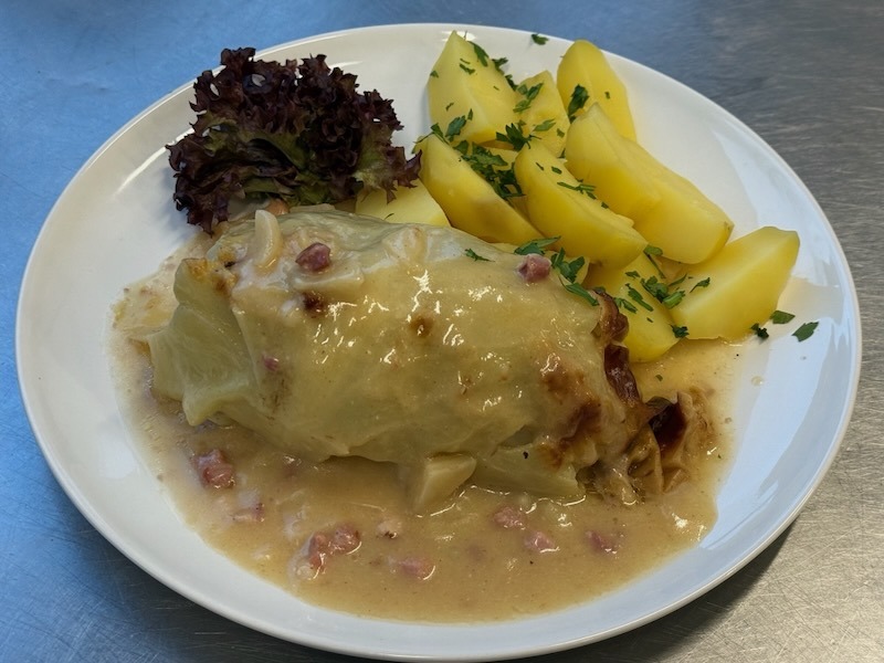 Caesar-Wrap mit Hähnchen, frischem Salat, Tomaten und Champignons, angerichtet auf einem Teller in der Hofküche auf Gut Tangstedt.