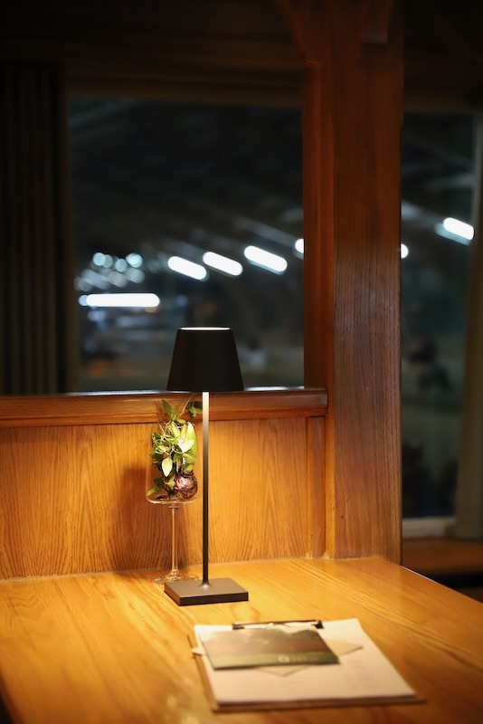 Gemütliche Abendstimmung im Bar-Bistro mit einer modernen Tischlampe auf einem Holztisch und stimmungsvollem Blick durch das Fenster.