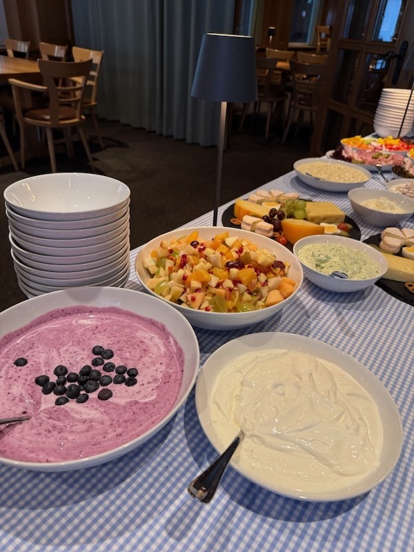 Reichhaltiges Frühstücksbuffet mit Schalen voller Blaubeerjoghurt, Naturjoghurt und frischem Obstsalat, ergänzt durch verschiedene Käseplatten in einem Restaurantambiente.