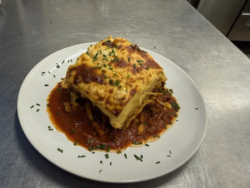 Griechischer Nudelauflauf Pastitsio mit Hackfleisch, Röhrennudeln und einer dicken Schicht Béchamelsauce, serviert auf einem weißen Teller.