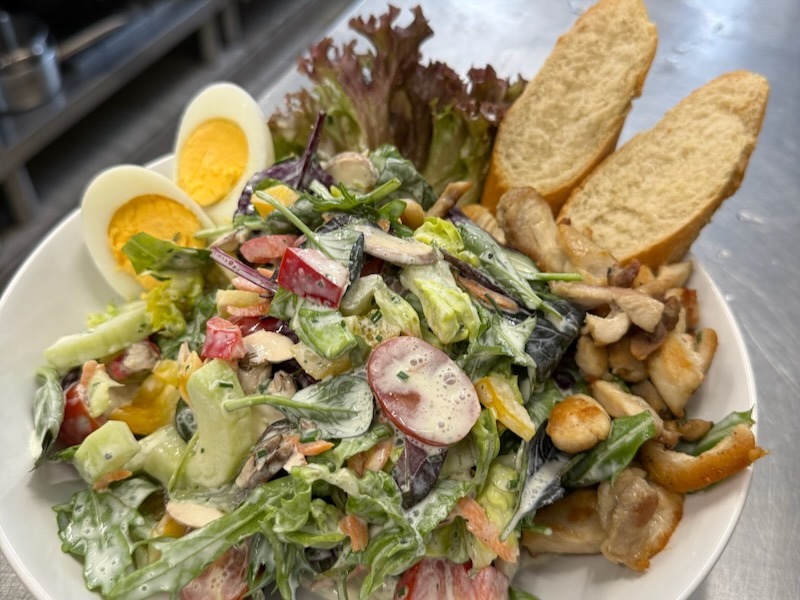 Salatteller mit gemischten Blattsalaten, Tomate, Paprika, Gurke, Karotten, ein hart gekochtes Ei und hausgemachtes Orangen- oder Joghurtdressing; dazu Brot