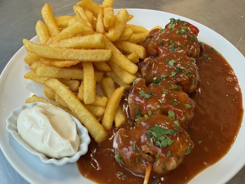 erzhafter Fleischspie&szlig; mit pikanter Schaschliksauce, serviert mit goldgelben Pommes frites und einem Klecks Mayonnaise auf einem wei&szlig;en Teller.