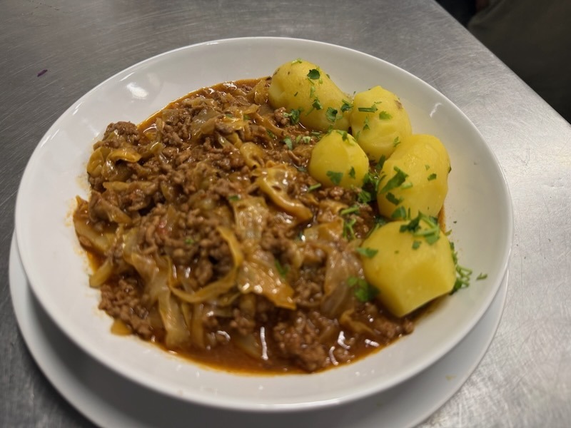 Klassischer Schmorkohl mit Hackfleisch in einer herzhaften Sauce, serviert mit Petersilienkartoffeln in einer wei&szlig;en Schale.