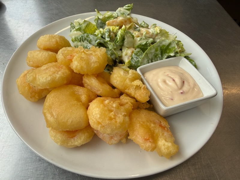 Knusprig frittierte Tempura-Garnelen, serviert mit einem cremigen Dip und einer frischen Blattsalat-Beilage auf einem weißen Teller.