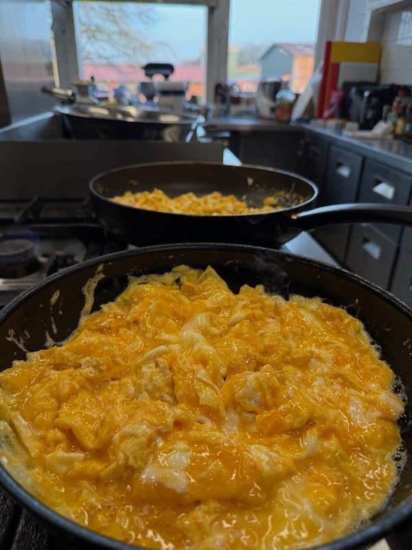 Frische Zubereitung von luftigem Rührei in einer Pfanne auf einem Gasherd in der Hofküche.