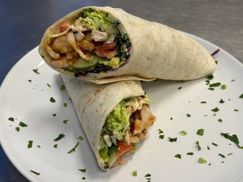 Herzhaft gefüllter Chicken Wrap mit saftigem Hähnchen, knackigem Salat, Tomaten und Gurken, appetitlich serviert auf einem weißen Teller.