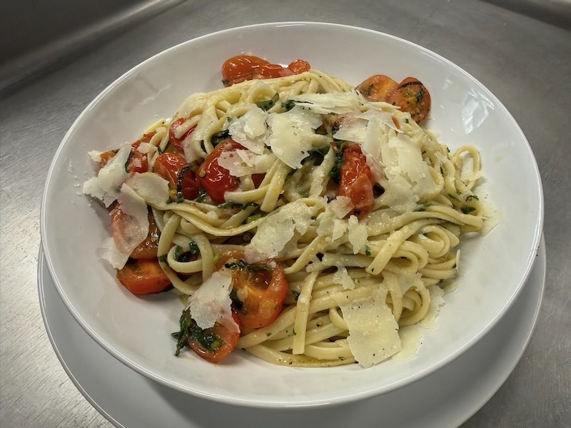 Frisch zubereitete Linguine aglio e olio mit aromatischen Kirschtomaten, frischen Kr&auml;utern und gro&szlig;z&uuml;gigen Parmesanhobeln, serviert in einer wei&szlig;en Schale.