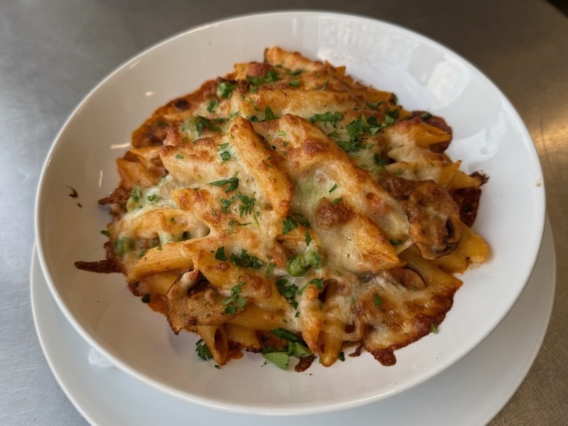 Frisch aus dem Ofen: Maccheroni al forno mit einer knusprigen K&auml;seschicht, verfeinert mit Erbsen und frischer Petersilie.