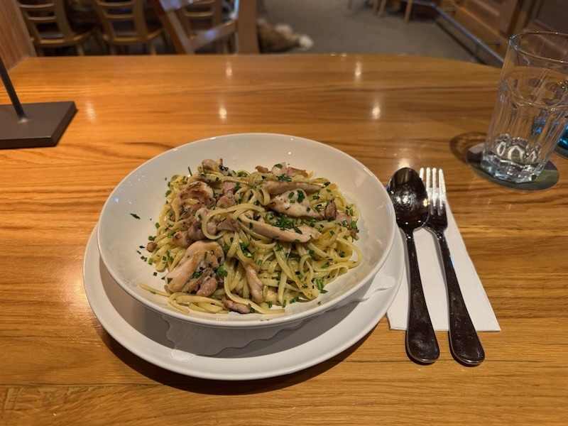 Nudeln mit gebratenem Hühnchen.jpg: Hausgemachte Pasta mit goldbraun gebratenen Hähnchenbruststücken und frischem Schnittlauch, appetitlich serviert in einer weißen Schale auf einem Holztisch.