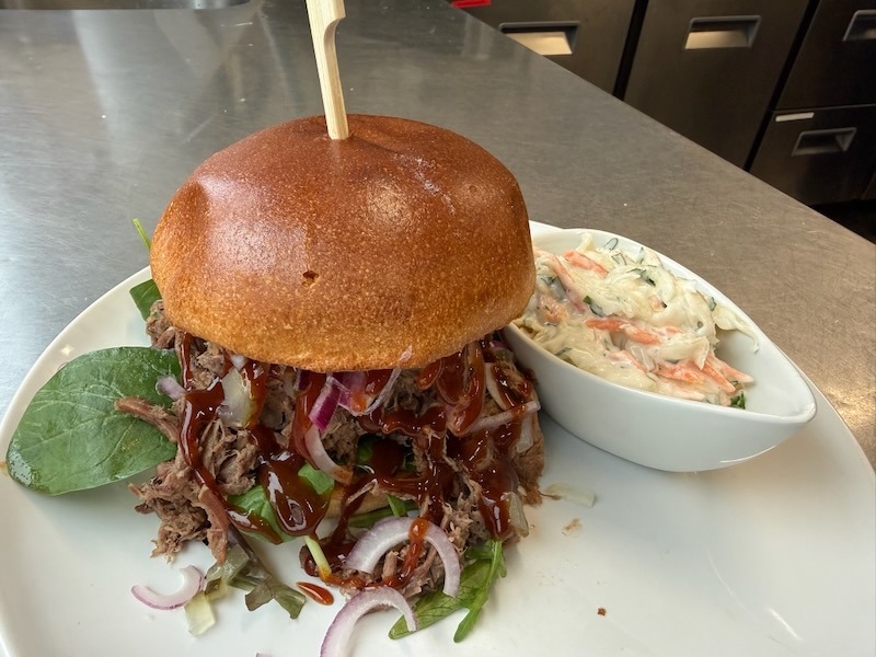 Ein herzhafter Pulled Beef Burger mit viel Sauce, roten Zwiebelringen und Salat, dazu eine Beilage aus hausgemachtem Coleslaw.