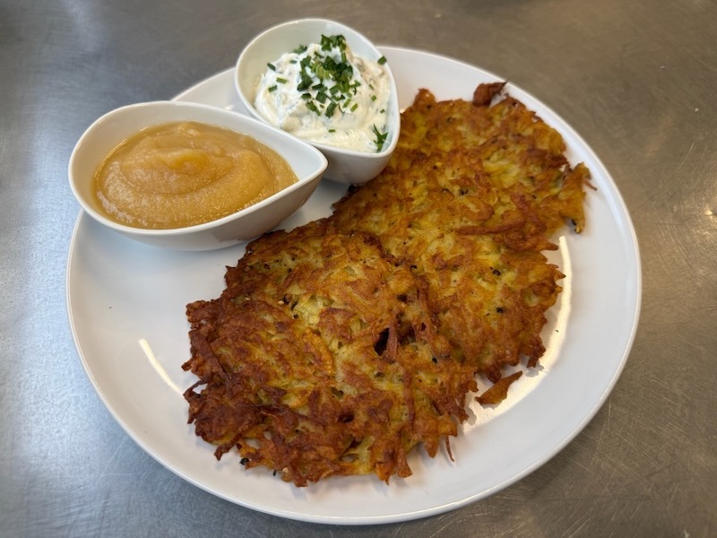 Drei goldbraun gebackene, knusprige Reibekuchen, serviert mit Apfelmus und Kräuterquark auf einem weißen Teller.