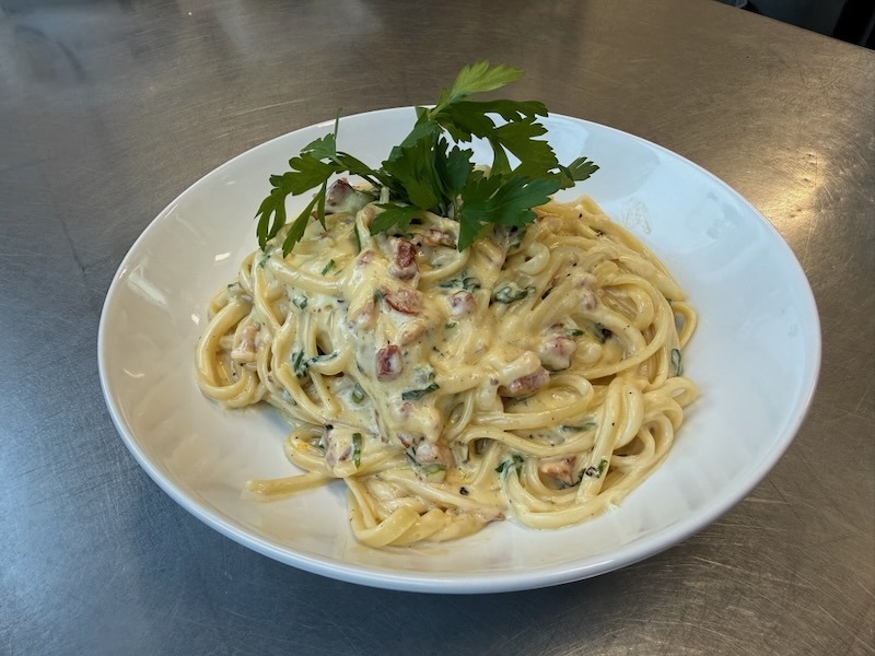 Cremige Spaghetti Carbonara mit knusprigen Speckw&uuml;rfeln und frischer Petersilie, serviert in einer tiefen wei&szlig;en Schale.