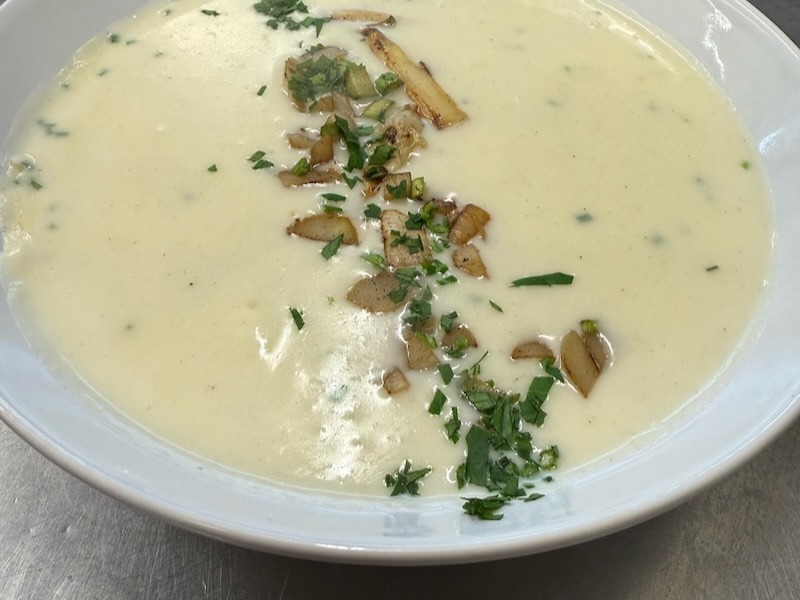 Cremige Spargelsuppe in einem tiefen wei&szlig;en Teller, garniert mit gebratenen Spargelst&uuml;cken, Fr&uuml;hlingszwiebeln und frisch gehackter Petersilie.