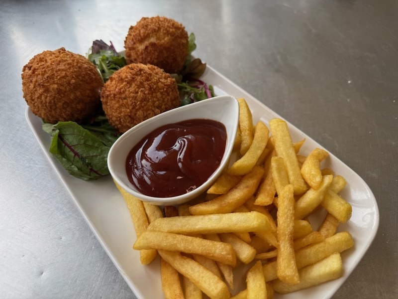 Drei knusprig panierte Pulled-Pork-Bällchen auf Blattsalat, serviert mit goldgelben Pommes frites und einem Schälchen BBQ-Sauce auf einem weißen Servierteller.