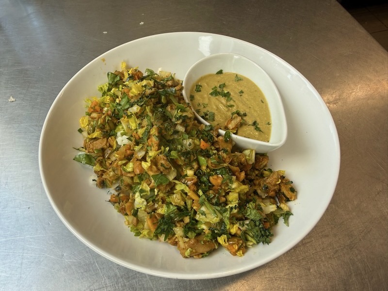 Crunchy Curry Chicken Bowl mit fein geschnittenem Hähnchen, Salat, Karotten und frischen Kräutern auf einem weißen Teller, dazu ein Schälchen cremige Erdnuss-Minz-Sauce