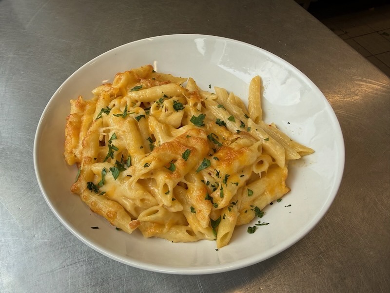 Überbackene Penne in cremiger Käsesauce mit goldbrauner Kruste, in einem tiefen weißen Teller serviert und mit frisch gehackter Petersilie bestreut.