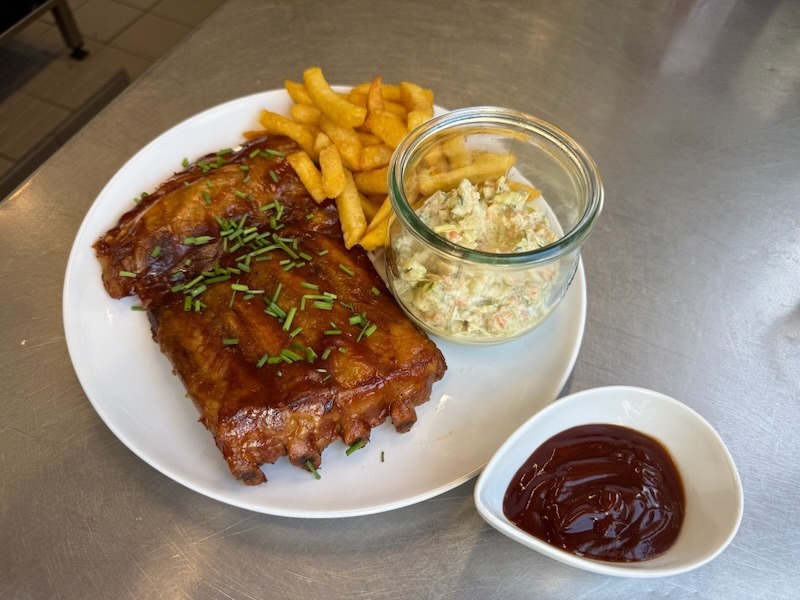 Glasierte Spare Ribs mit Schnittlauch auf einem weißen Teller, serviert mit Pommes frites, Coleslaw im Weckglas und einem Schälchen BBQ-Sauce.
