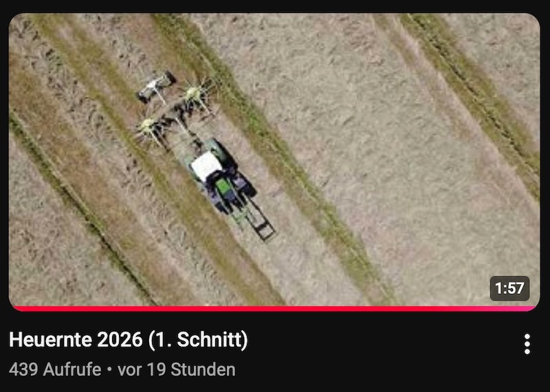 Luftaufnahme eines Traktors mit Kreiselheuer beim Wenden von Grünfutter auf einem abgemähten Feld, Standbild aus dem YouTube-Video "Heuernte 2026 (1. Schnitt)".