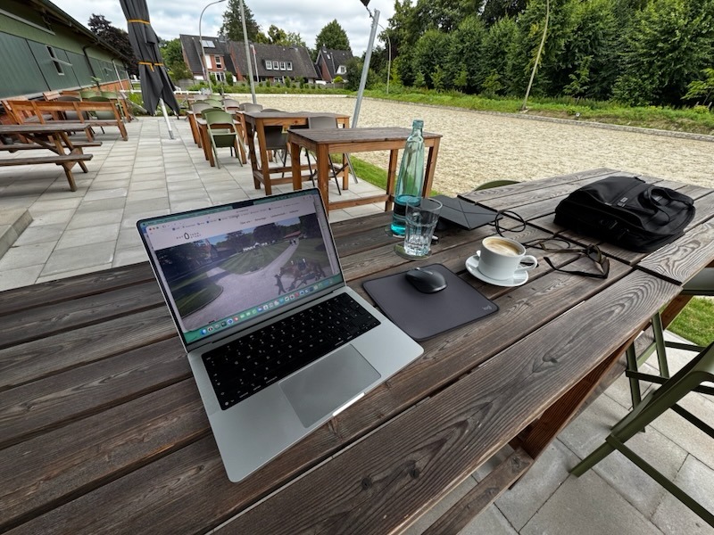 MacBook Pro und Kaffee aus der Hofküche auf einem Holztisch der Außenterrasse – Arbeiten im Freien auf Gut Tangstedt.