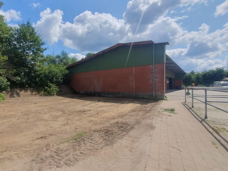 Vorbereitungsarbeiten für den Bau des Heizhauses auf Gut Tangstedt: Ein Radlader räumt alte Betonplatten neben der Backsteinmauer des Werkstattgebäudes beiseite, der Untergrund ist bereits freigelegt.
