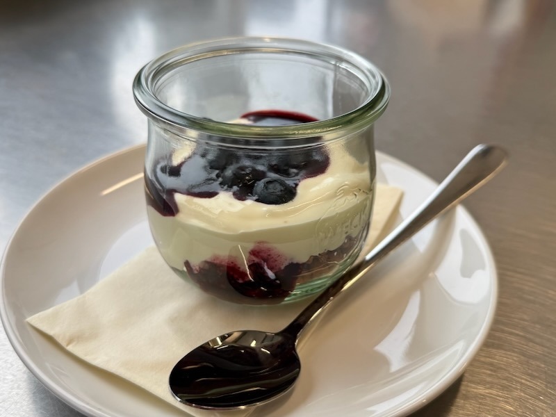Cheesecake im Weckglas mit cremiger Käsemasse und Blaubeerkompott, serviert auf einem weißen Unterteller mit Löffel.