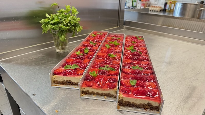 Käse-Erdbeerkuchen auf Blechen für ein Hochzeitscatering, garniert mit frischen Erdbeeren und Minze, in der Küche von Gut Tangstedt