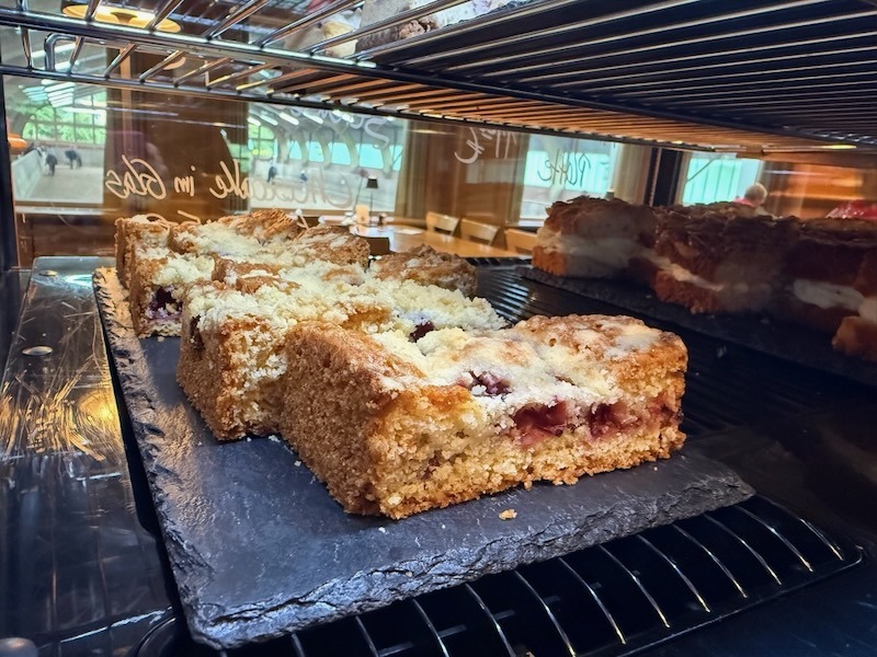 Saftige Kirsch-Streuselkuchen-Schnitten mit goldbraunen Streuseln auf einer Schieferplatte in der Kuchenvitrine der Hofk&uuml;che.