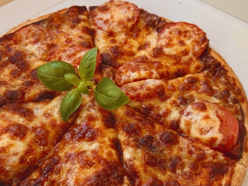 Knusprig gebackene Pizza Caprese mit Tomatensauce, geschmolzenem Mozzarella und Tomatenscheiben, garniert mit frischem Basilikum, in einem Pizzakarton.