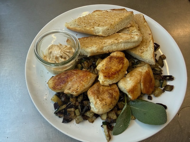 Gebratene H&auml;hnchen-Medaillons auf geschmortem Auberginen-Zucchini-Gem&uuml;se mit frischem Salbei, dazu ger&ouml;stetes Toastbrot und ein Weckglas mit Salbeibutter.