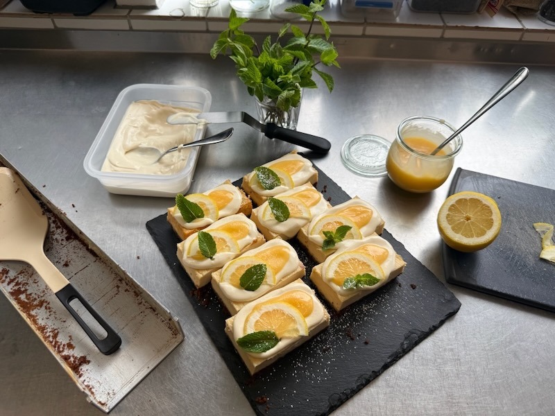 Frisch garnierte Lemon-Cheesecake-Schnitten mit Frischkäsecreme, Zitronenscheiben und Minze auf einer Schieferplatte – Blick hinter die Kulissen der Hofküche Gut Tangstedt.