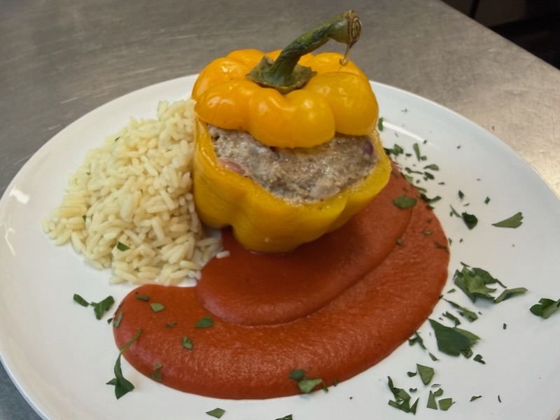 Würziges Gulasch mit Paprika und Tomaten in kräftiger Sauce auf einem weißen Teller, serviert mit Salzkartoffelspalten und frischer Petersilie.