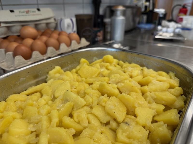 Frisch angemachter Kartoffelsalat in einer Edelstahlschale in der Hofk&uuml;che von Gut Tangstedt, dahinter braune Eier im Eierkarton