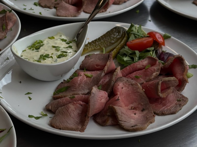 Rosa gebratenes Roastbeef in d&uuml;nnen Scheiben, dazu Remoulade im Sch&auml;lchen, Gew&uuml;rzgurke und Salat mit Kirschtomaten, mit Petersilie bestreut auf wei&szlig;em Teller in der Hofk&uuml;che von Gut Tangstedt